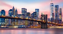Manhattan skyline at dusk, lit up, intersected by the Brooklyn Bridge