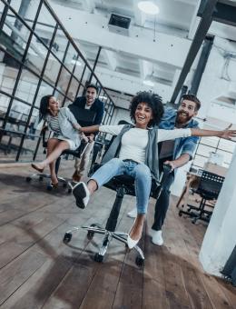 Deux femmes font la course, poussées par leur collègues sur des chaises de bureaux roulantes. 