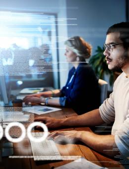 A man and a woman working at computers with visible data 