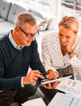A man and a woman discussing finance using a tablet, surrounded by financial documents