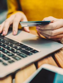 A person's hands are visible using a laptop and holding a bank card, the person wears a yellow top