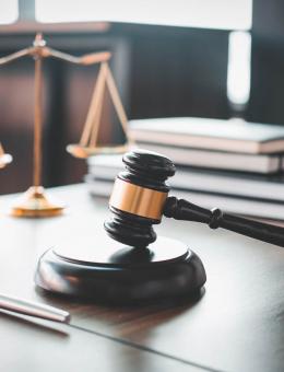 A gavel resting on a desk with scales and books in the background
