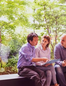 A man pointing to a document heald by a woman with another man next to her holding a tablet