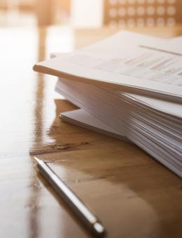 A pile of document on an office desk with a pair of glasses and some pens